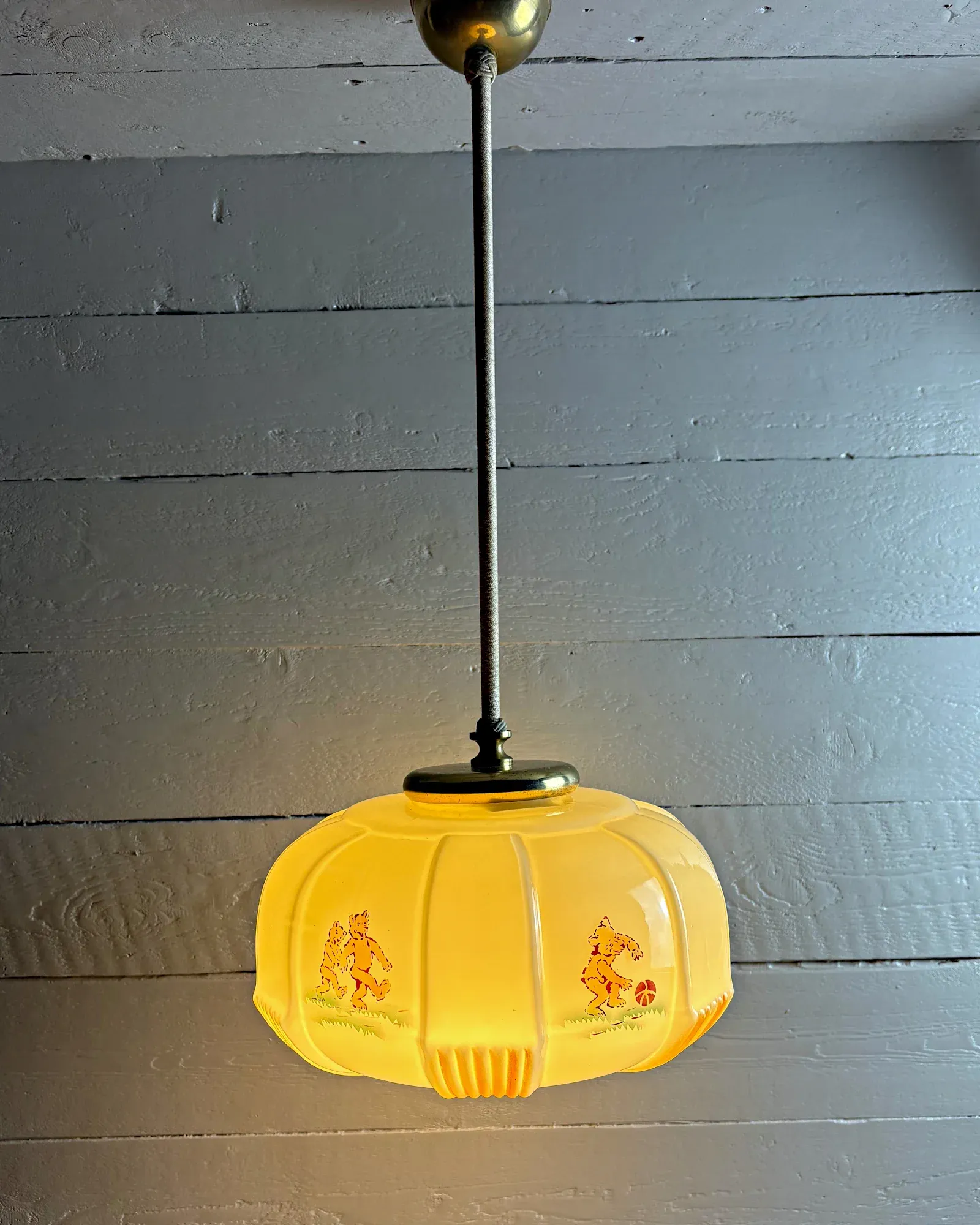 Opal glass children's pendant lamp with printed bears and brass fittings, hanging on a rod, front view