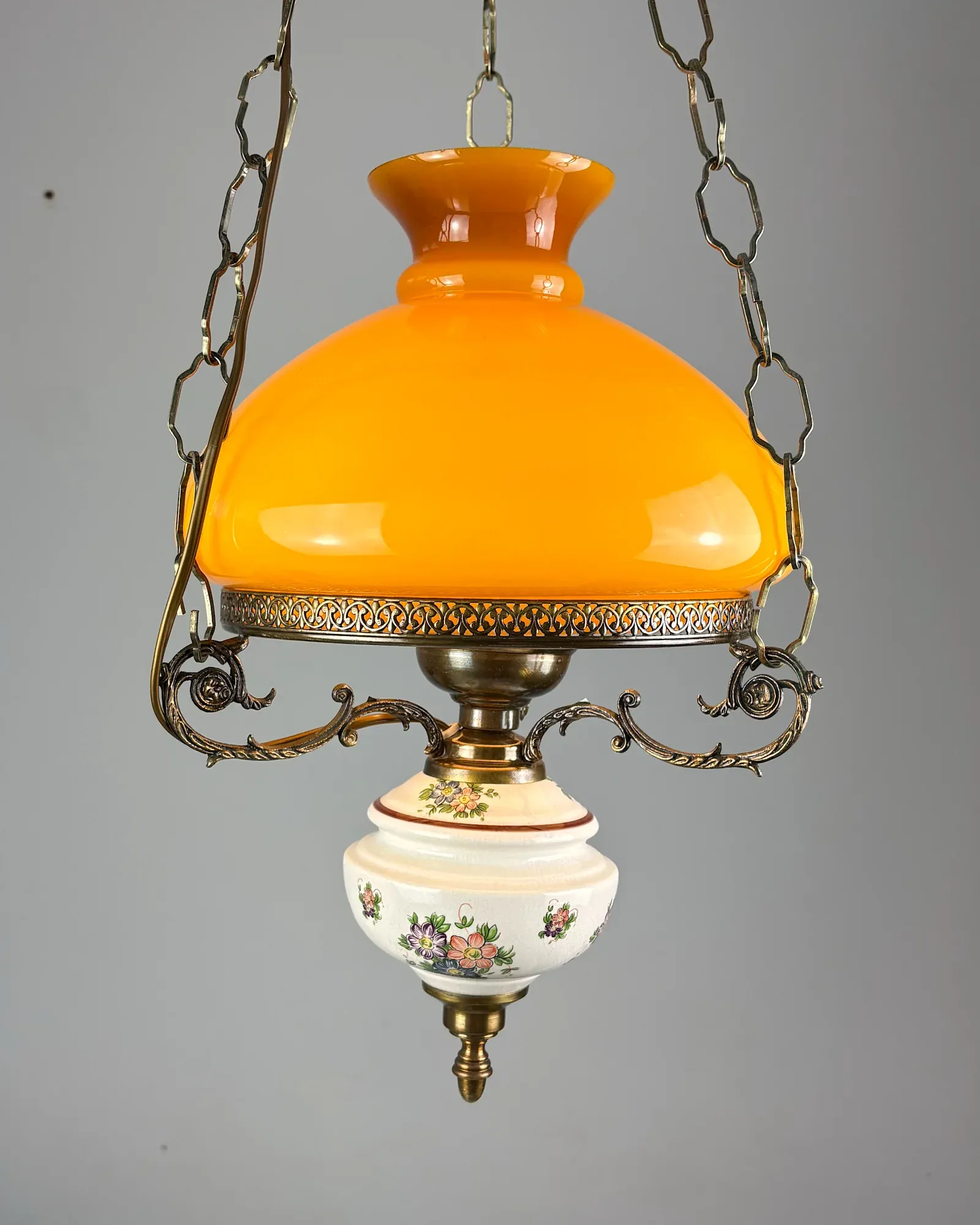 Oil lamp style brass pendant light with amber opal glass shade and floral ceramic font, front view