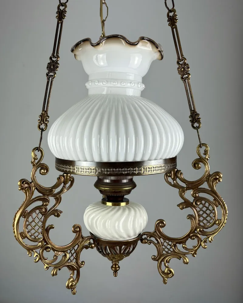Three-quarter view of the brass hanging oil lamp with pierced Rococo scrollwork arms and milk glass shade