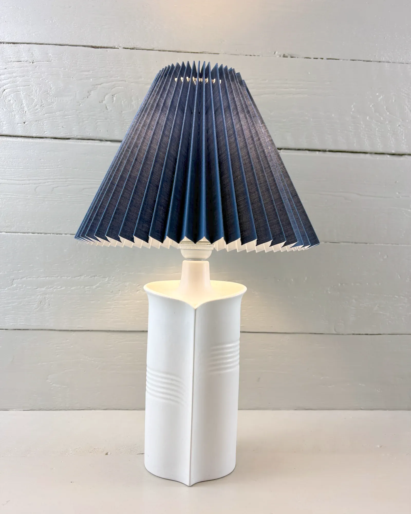 White Soholm ceramic table lamp model 1229 by Maria Philippi, front view, with an illustrative blue pleated shade
