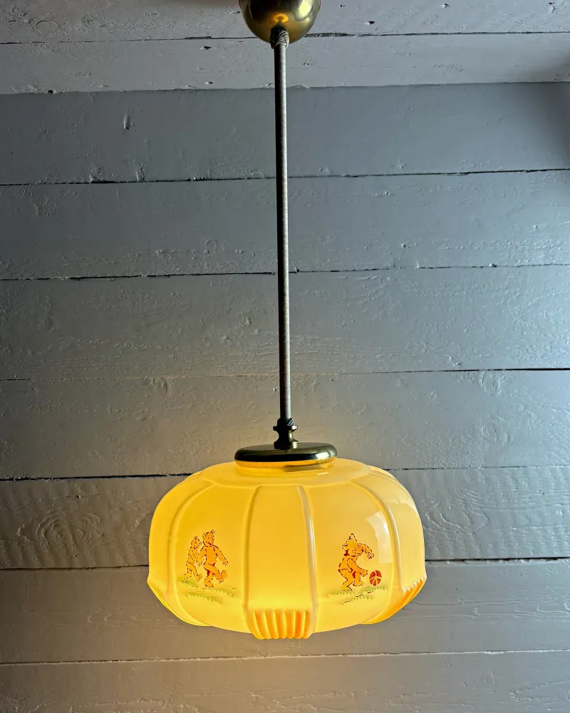 Opal glass children's pendant lamp with printed bears and brass fittings, hanging on a rod, front view