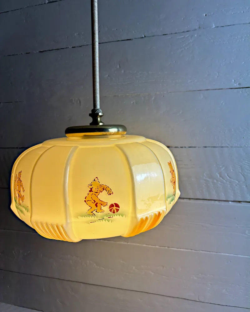 Cream opal glass pendant shade with six moulded panels and a printed bear kicking a ball, three-quarter view