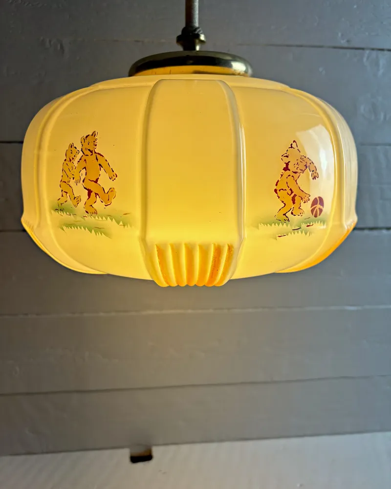 Lit opal glass shade with printed bear scenes in amber and brown, brass cap and textile-wrapped rod above