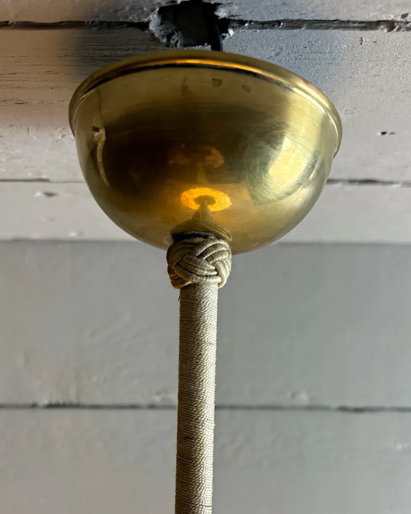 Brass domed ceiling canopy of the pendant lamp with a knotted cover and a thread-wrapped rod below