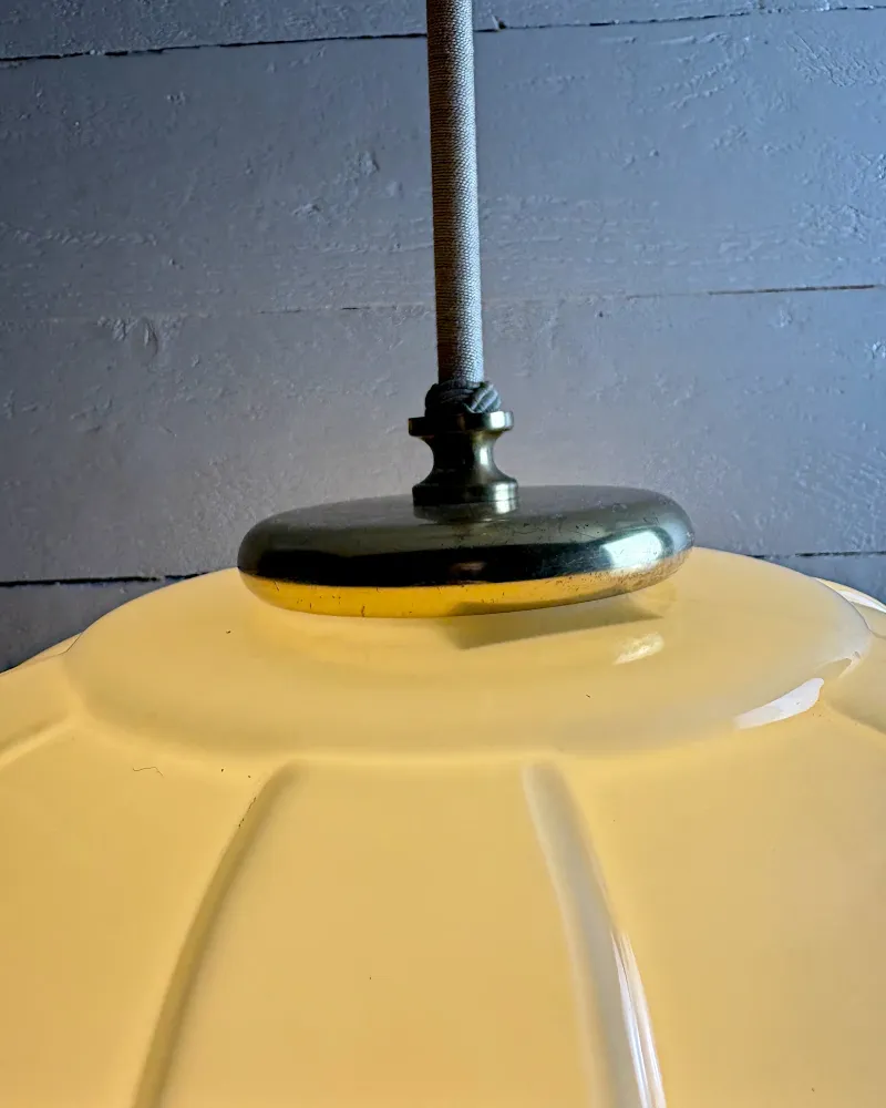 Flat brass cap on the shoulder of the opal glass shade where the textile-wrapped rod enters the lamp