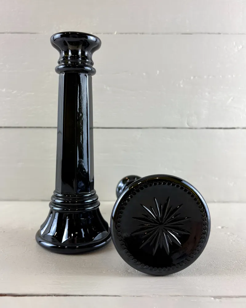 Black glass column candlestick standing beside its pair laid on its side to show the starburst underside