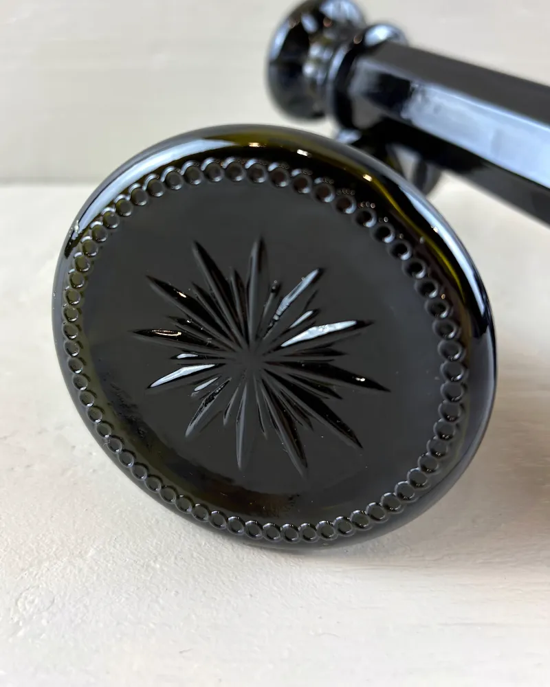 Pressed starburst motif framed by a beaded border on the underside of a black glass candlestick base
