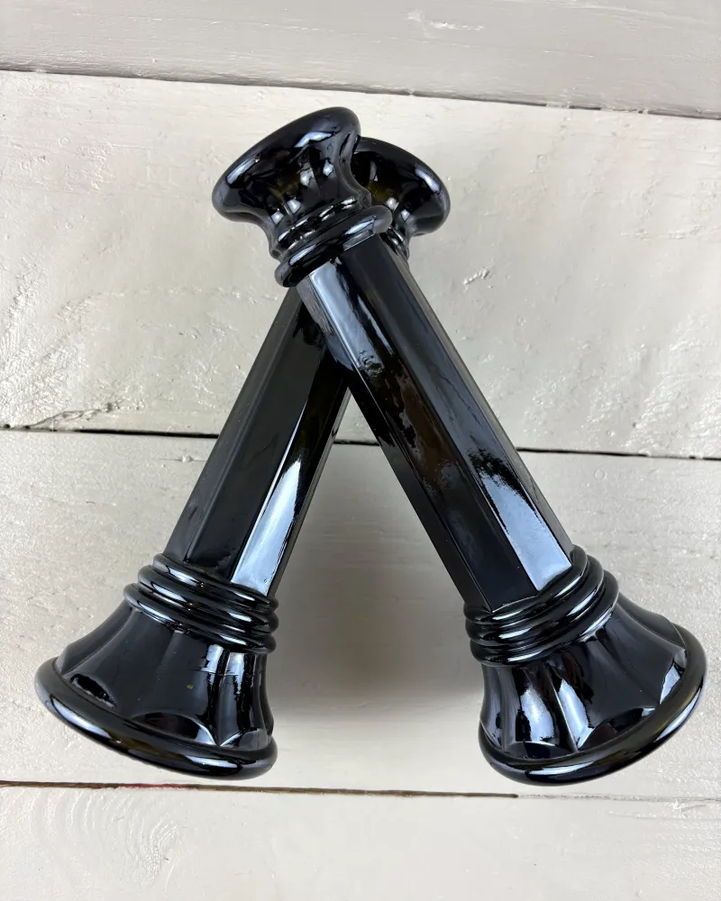 Two black glass candlesticks leaning crosswise, showing the faceted octagonal shafts and ringed bases