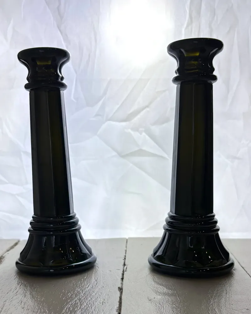 Backlit pair of black glass column candlesticks revealing the dark olive green colour of the glass