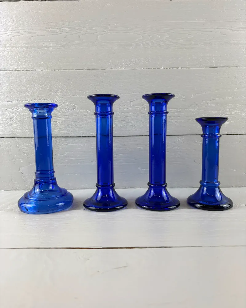 Set of four cobalt blue glass candlesticks in graduated heights, front view on white painted boards