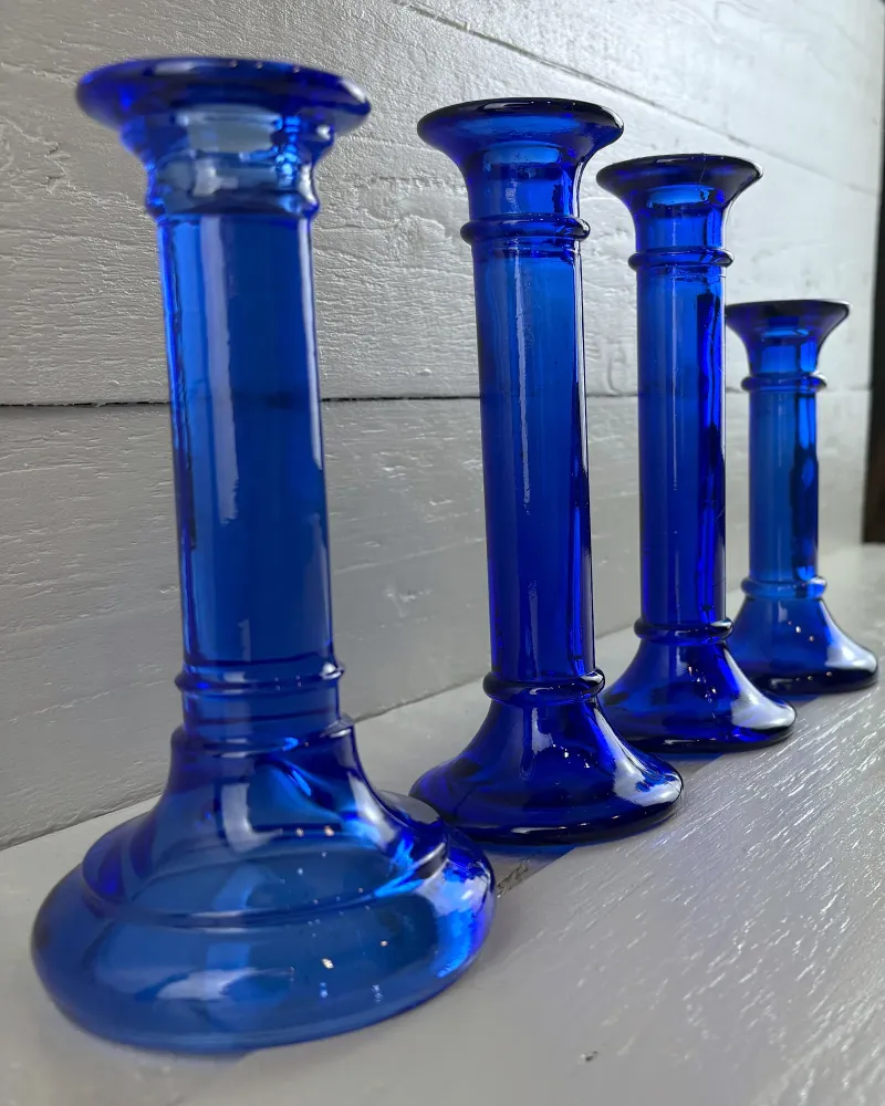 Four cobalt blue glass candlesticks in a row seen at an angle, with ringed stems and flared cups