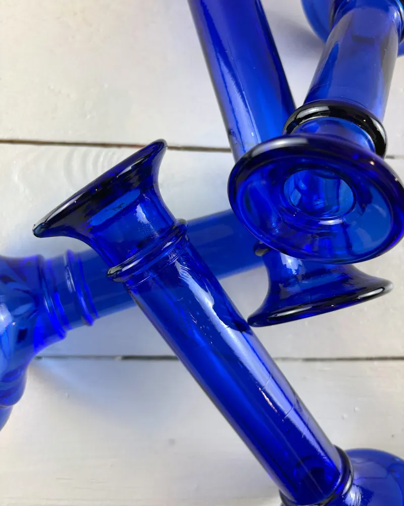 Flared rim, ring and stem of cobalt blue glass candlesticks lying on white boards, with small bubbles