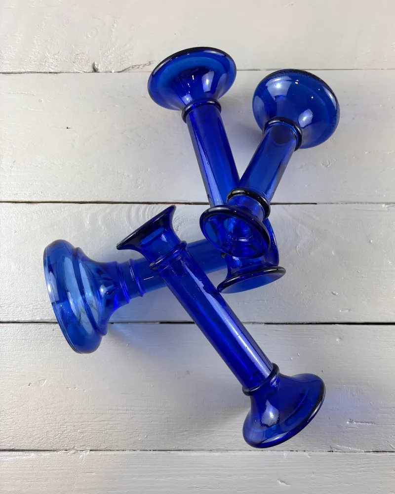Four cobalt blue glass candlesticks lying on white boards, showing their flared candle cups and domed feet