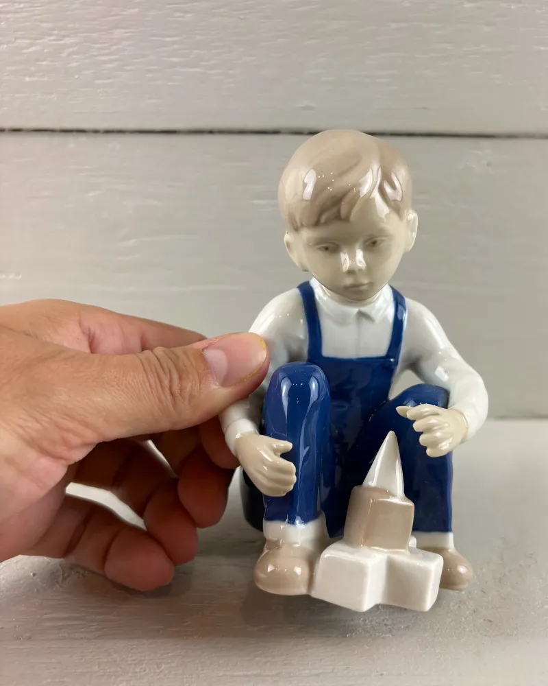 Hand holding a porcelain figurine of a boy with building blocks, showing its size