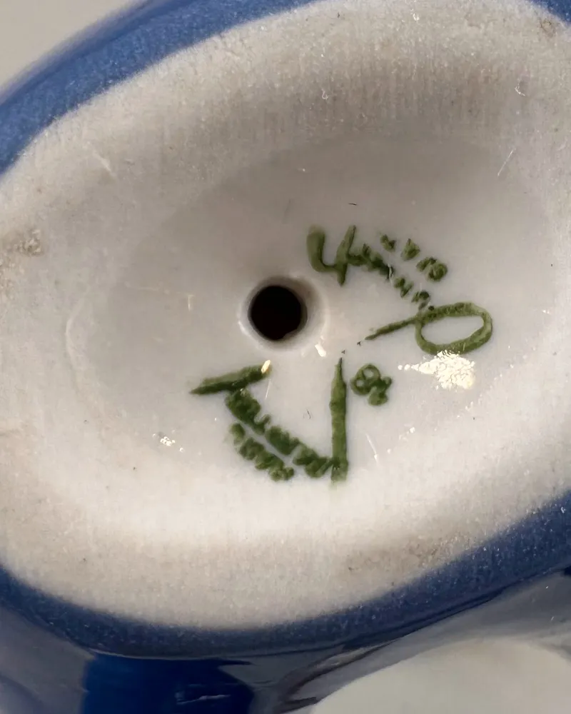Close-up of green marks on the unglazed base of a porcelain figurine of a boy with building blocks