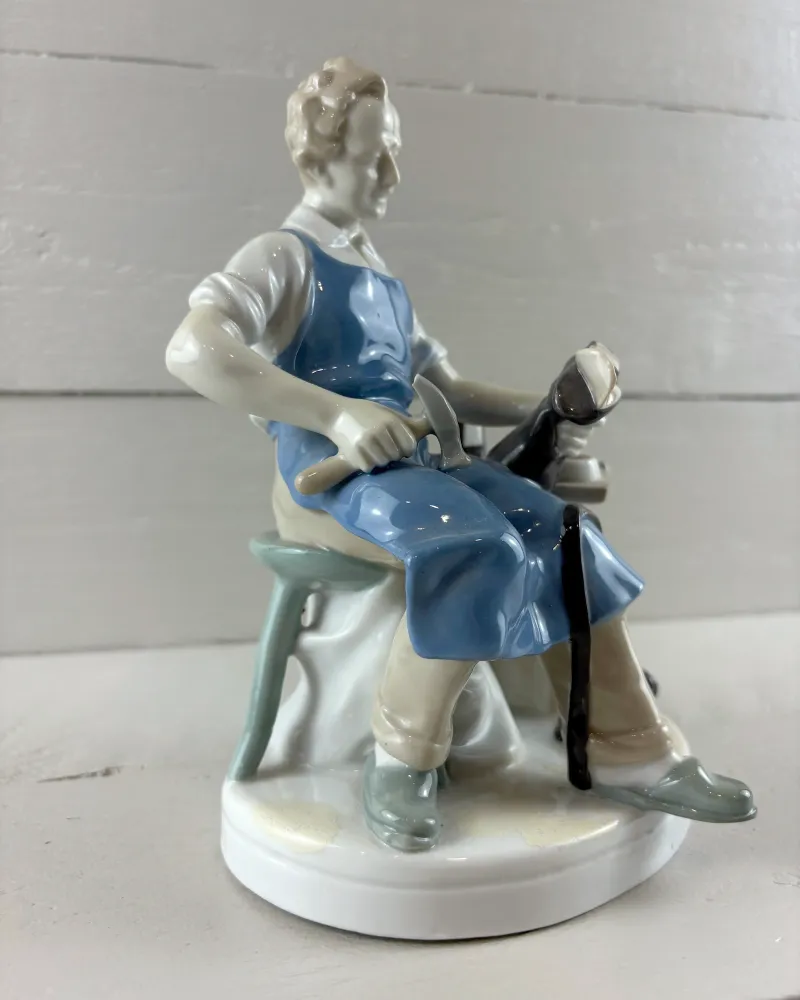 Grafenthal porcelain cobbler figurine, three-quarter view of the seated shoemaker on a green three-legged stool