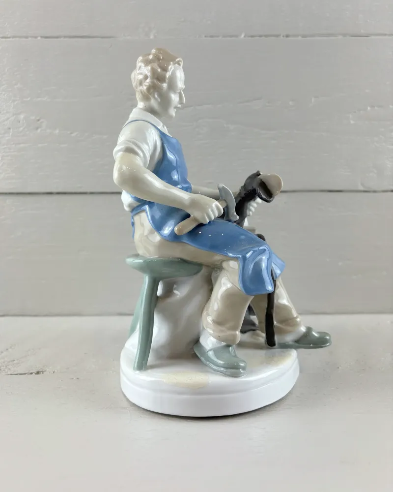 Left side profile of a hand-painted Grafenthal porcelain cobbler hammering a boot held on his knee