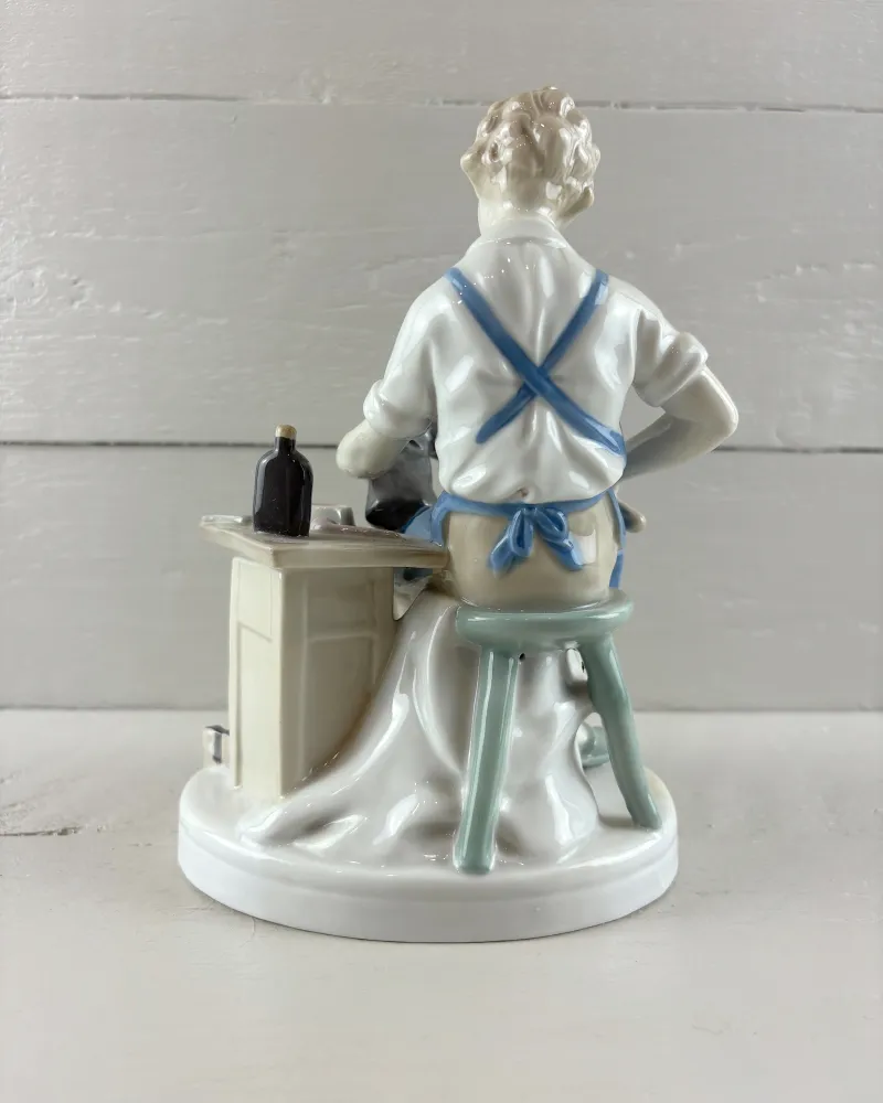 Back of the Grafenthal porcelain cobbler figurine showing crossed blue apron straps and the cream workbench