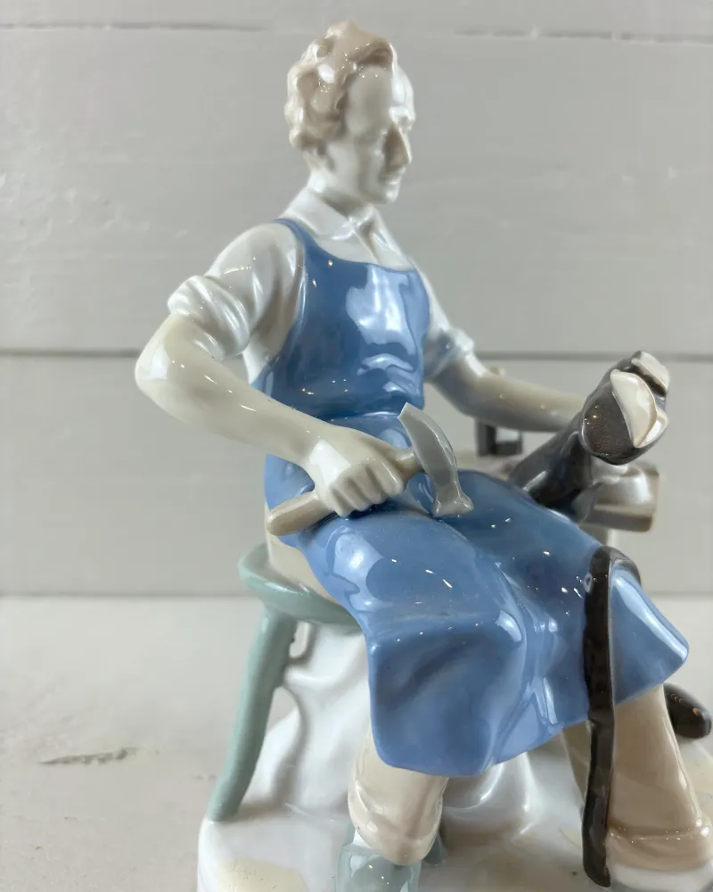 Close-up of the Carl Scheidig cobbler figurine: face, glossy blue apron and hand holding a hammer