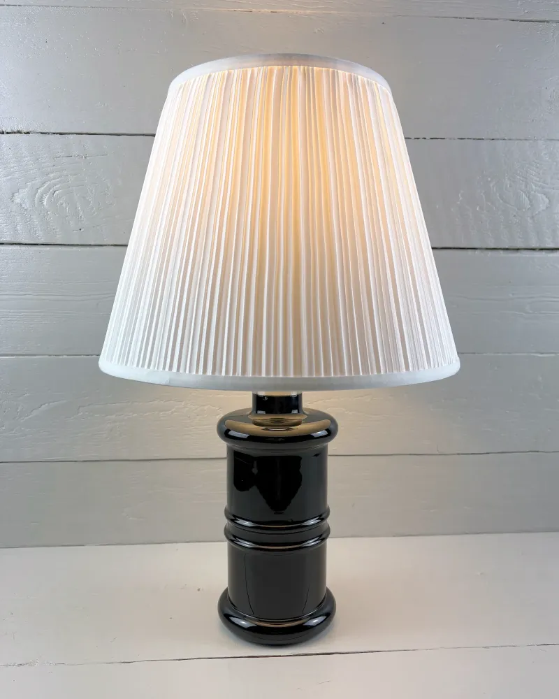 Holmegaard Apotheker black glass table lamp with a pleated shade, front view; shade is illustrative only