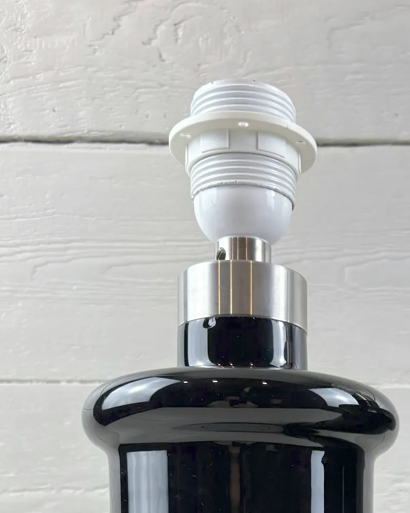 Close-up of the satin metal collar and white lamp socket on a Holmegaard Apotheker black glass base