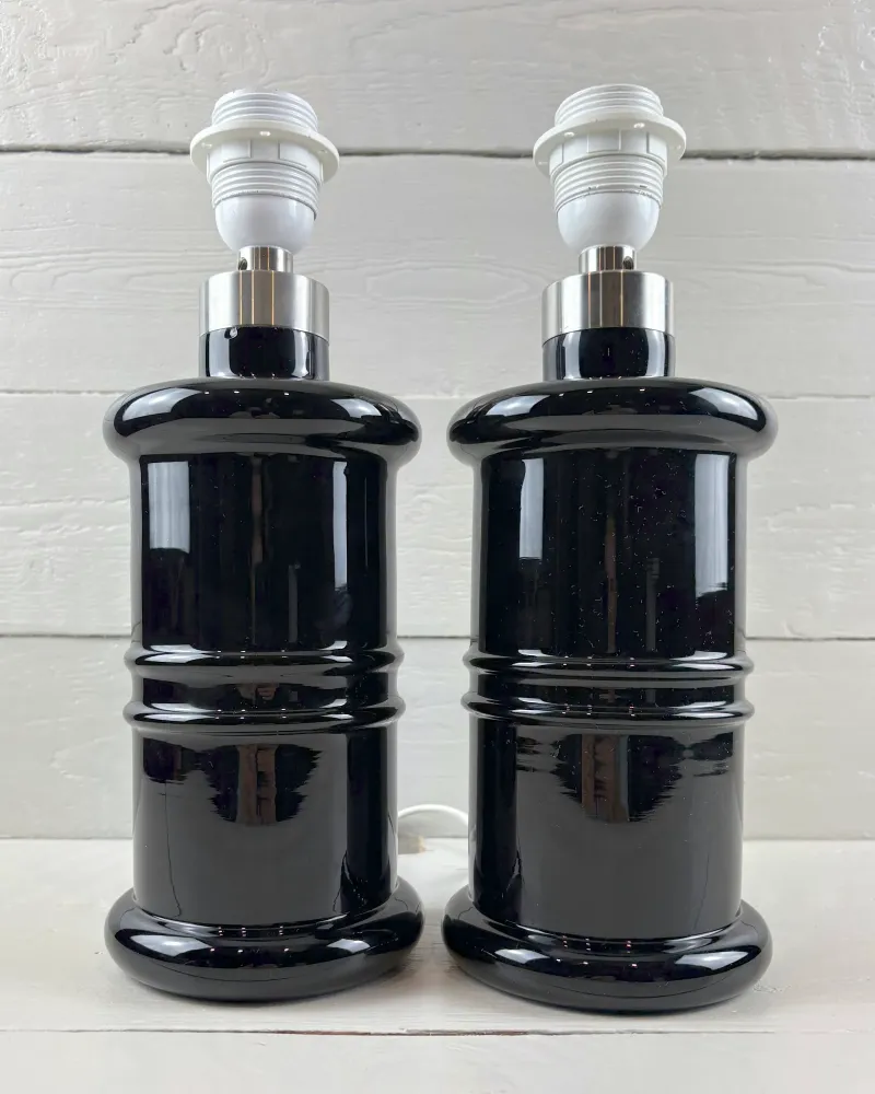 Close-up of two Holmegaard Apotheker black glass lamp bases with metal collars and ridged rings, no shades
