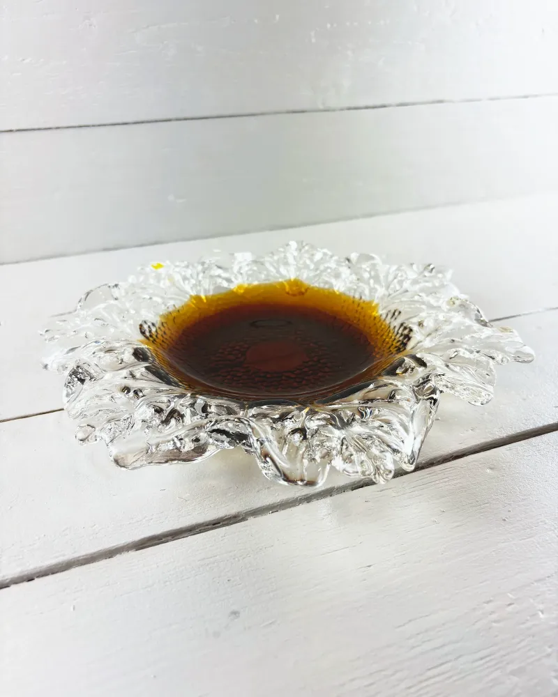 Kasvimaalla bowl by Humppila seen at a low three-quarter angle, showing the curled clear glass leaves around the amber well