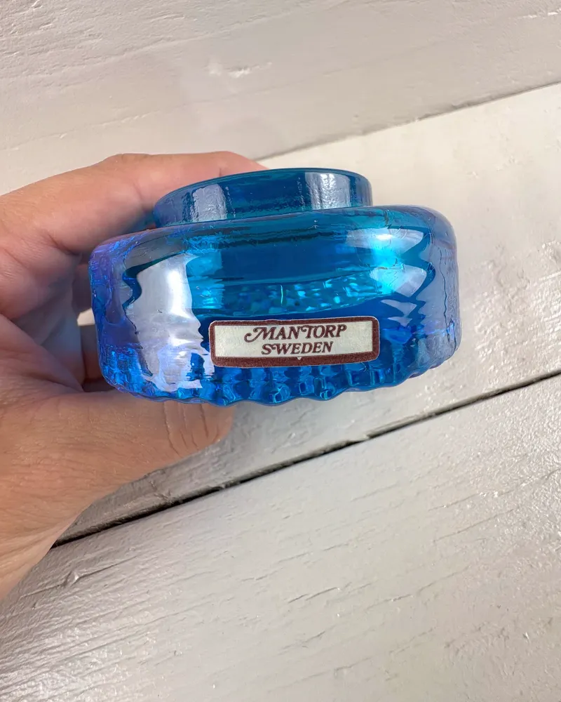 Assembled Mantorp blue glass paperweight held in a hand to show its size, with Mantorp Sweden label
