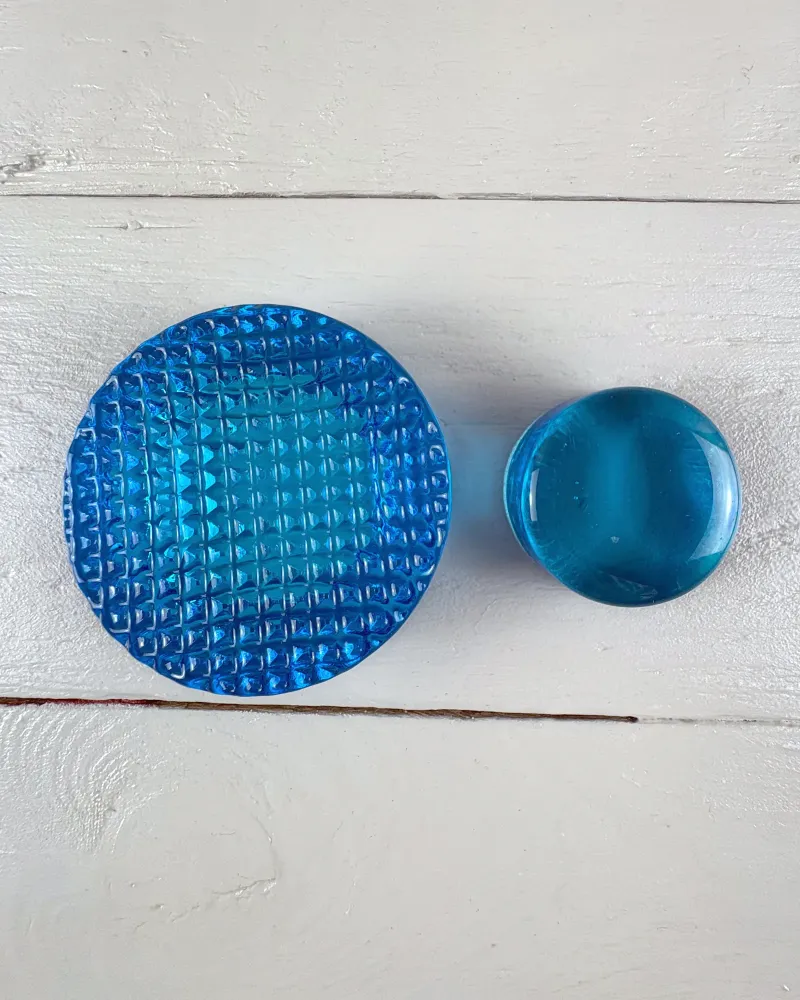 Underside of the Mantorp blue glass paperweight with a grid of pyramid studs, beside the domed glass disc
