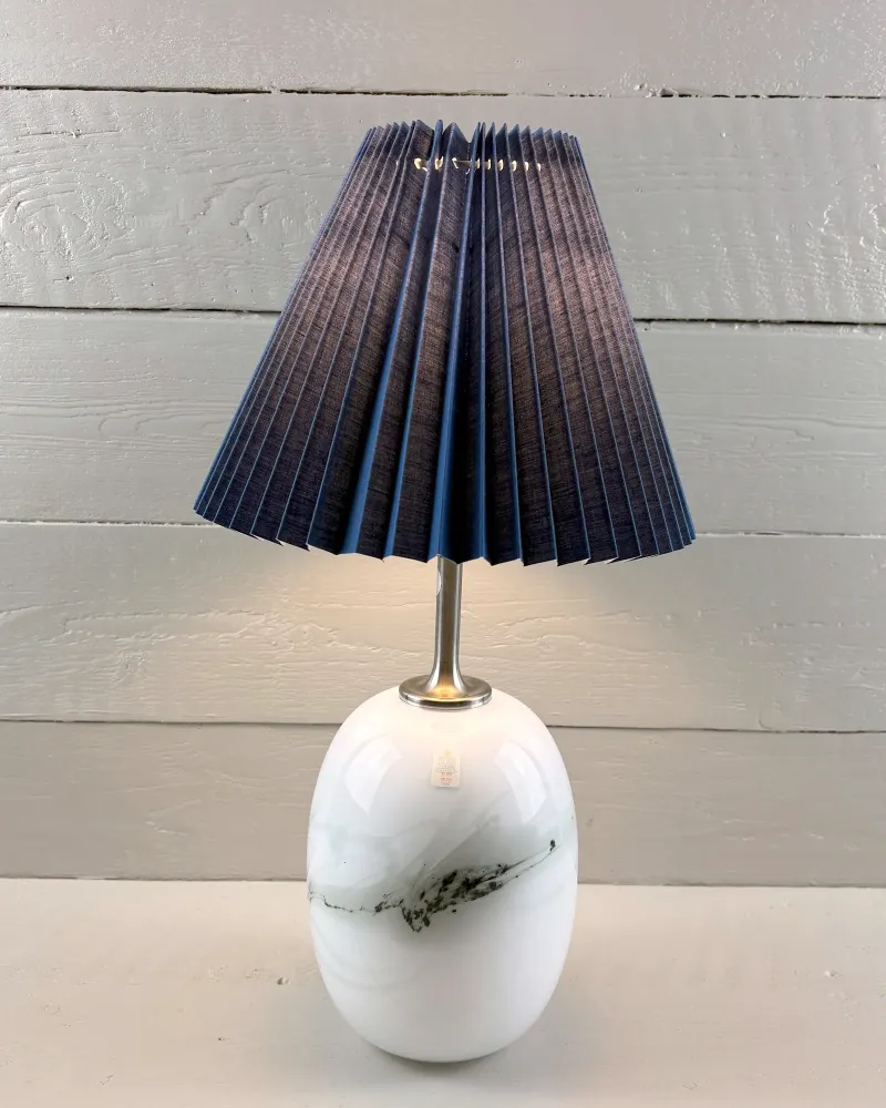 Holmegaard Sakura lamp by Michael Bang shown with an illustrative blue pleated shade, not included