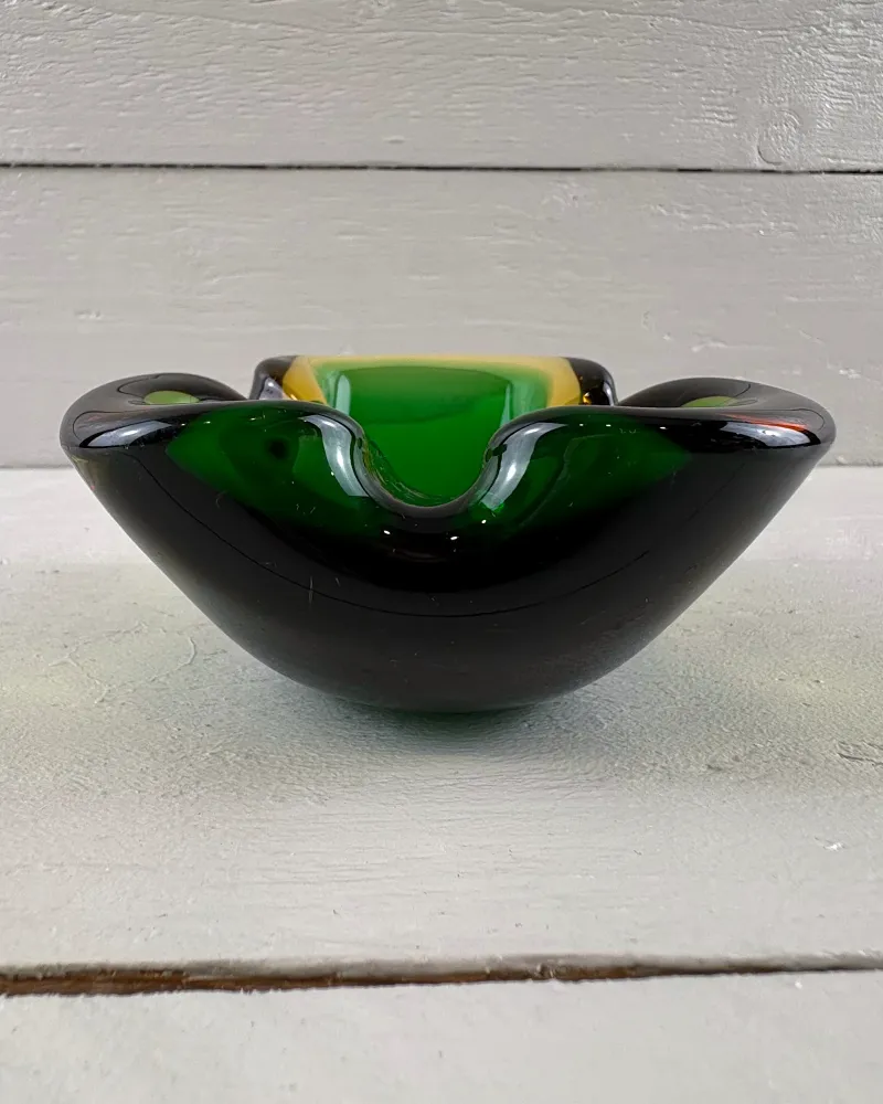 Side profile of a Murano-style sommerso glass ashtray with a deep rounded body and notched rim