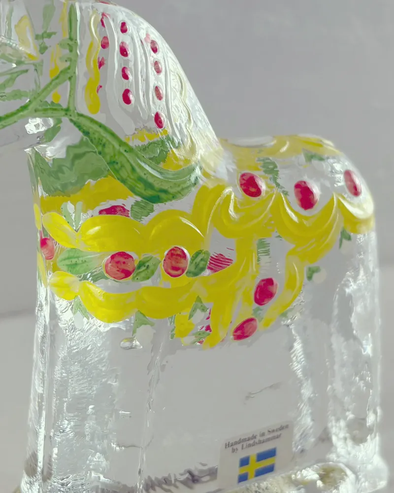 Close-up of the hand-painted yellow garland and red berries on a clear glass Dala horse by Lindshammar