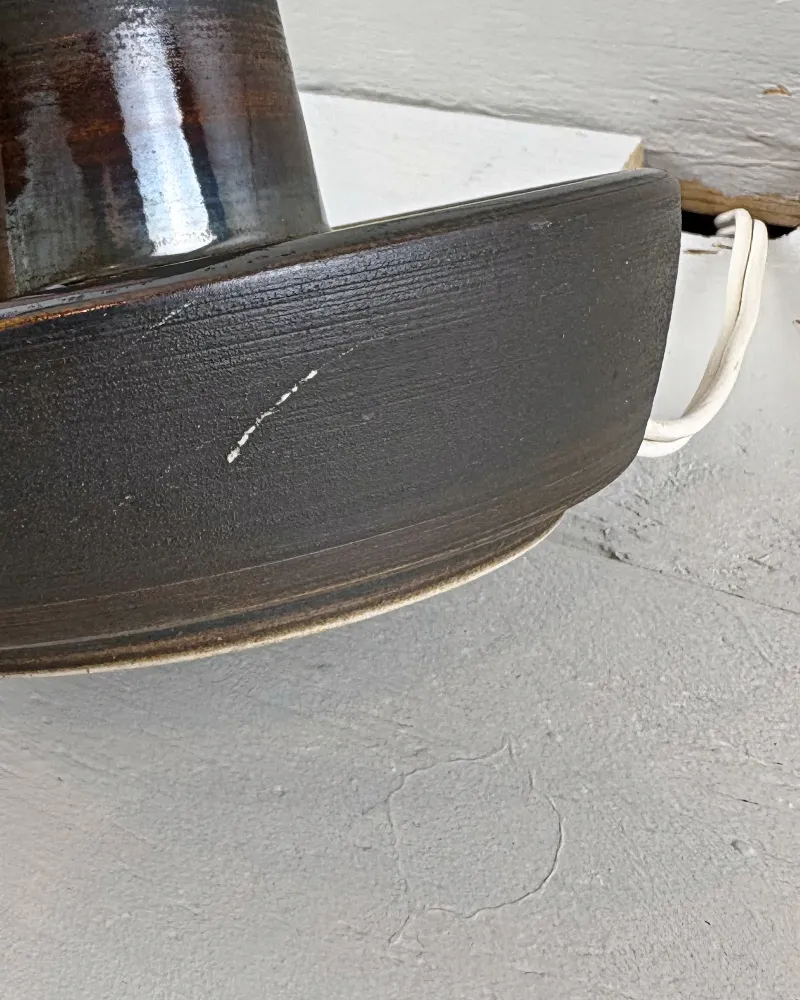 Side of Soholm 1072 lamp bowl with a thin pale scratch across the matte dark stoneware, cord at right